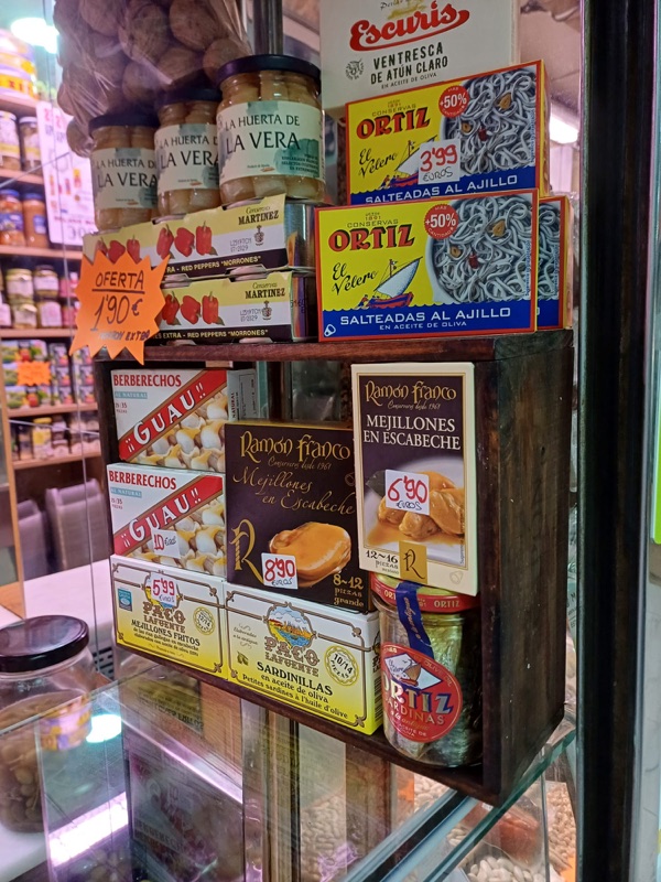 Estantería del puesto con conservas selectas: ventresca y sardinillas Ortiz, mejillones y berberechos Ramón Franco, anchoas La Huerta de La Vera.