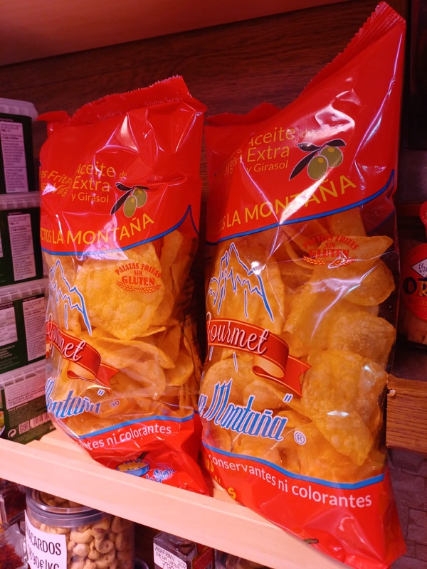 Bolsas de patatas fritas gourmet La Montaña, fritas en aceite extra de girasol, en una estantería del puesto.