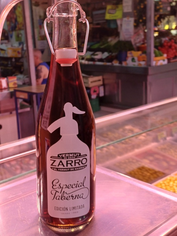 Botella de Vermut Zarro Especial Taberna (edición limitada, desde 1968) sobre el mostrador del puesto, con el mercado al fondo.