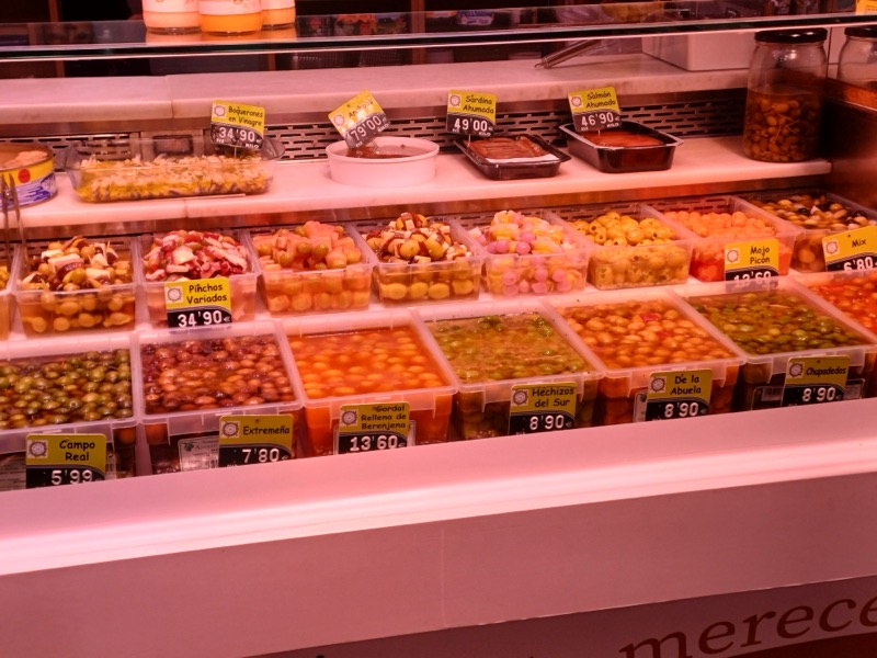 Vitrina del puesto con cubetas de aceitunas, gildas, banderillas variadas y pulpo a la vinagreta, con sus etiquetas de precio.